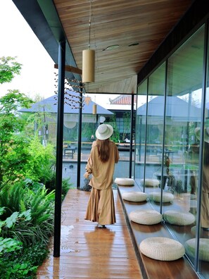 A person walking on a wooden deck with glass walls, overlooking a garden and a body of water. - Terra Art Zen Hotel (Chengdu)