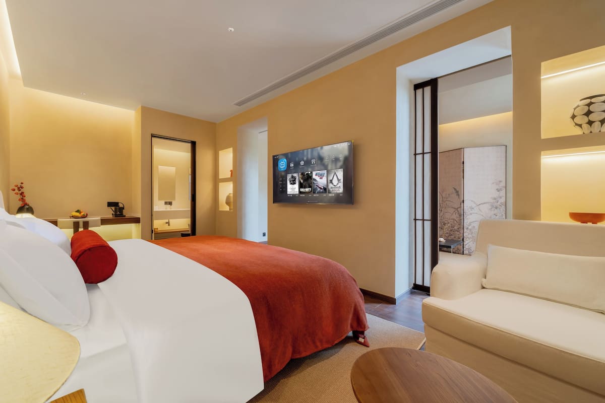 Una camera d'albergo con un letto, un divano, una TV e un'opera d'arte appesa al muro.
