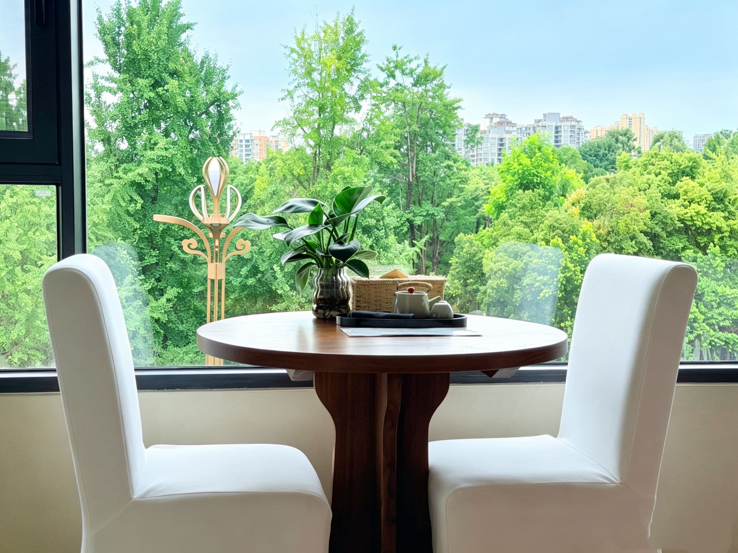A room with a round wooden table, two white chairs, a decorative metal sculpture, a potted plant, and a wicker basket with a teapot.