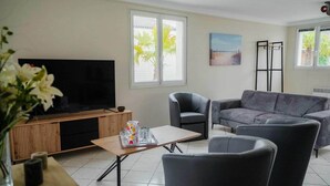 Un salon équipé d’un téléviseur à écran plat, d’un canapé gris, de fauteuils, d’une table basse et d’un meuble pour téléviseur.