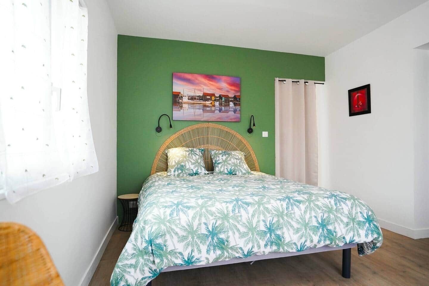 A bedroom with a bed, a green wall, a painting, and a red picture frame.