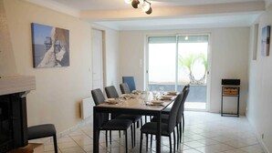 Un coin repas avec une grande table dressée pour six personnes, une cheminée et une vue sur l’extérieur.
