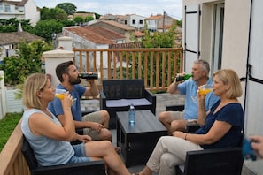 Un groupe de personnes est assis sur des meubles de jardin, autour d’une table et de chaises. On aperçoit une bouteille d’eau et un verre de jus d’orange.