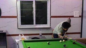 Une table de billard avec des billes, une fenêtre et un mur orné d’un motif de marbre.