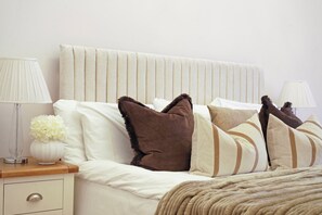 A neatly made bed with a striped headboard, a bedside table with a lamp, and a vase with flowers. - Understated Luxury Flat in Mayfair (London)