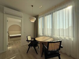 A modern dining area with a round table, black chairs, and a large window with sheer curtains.