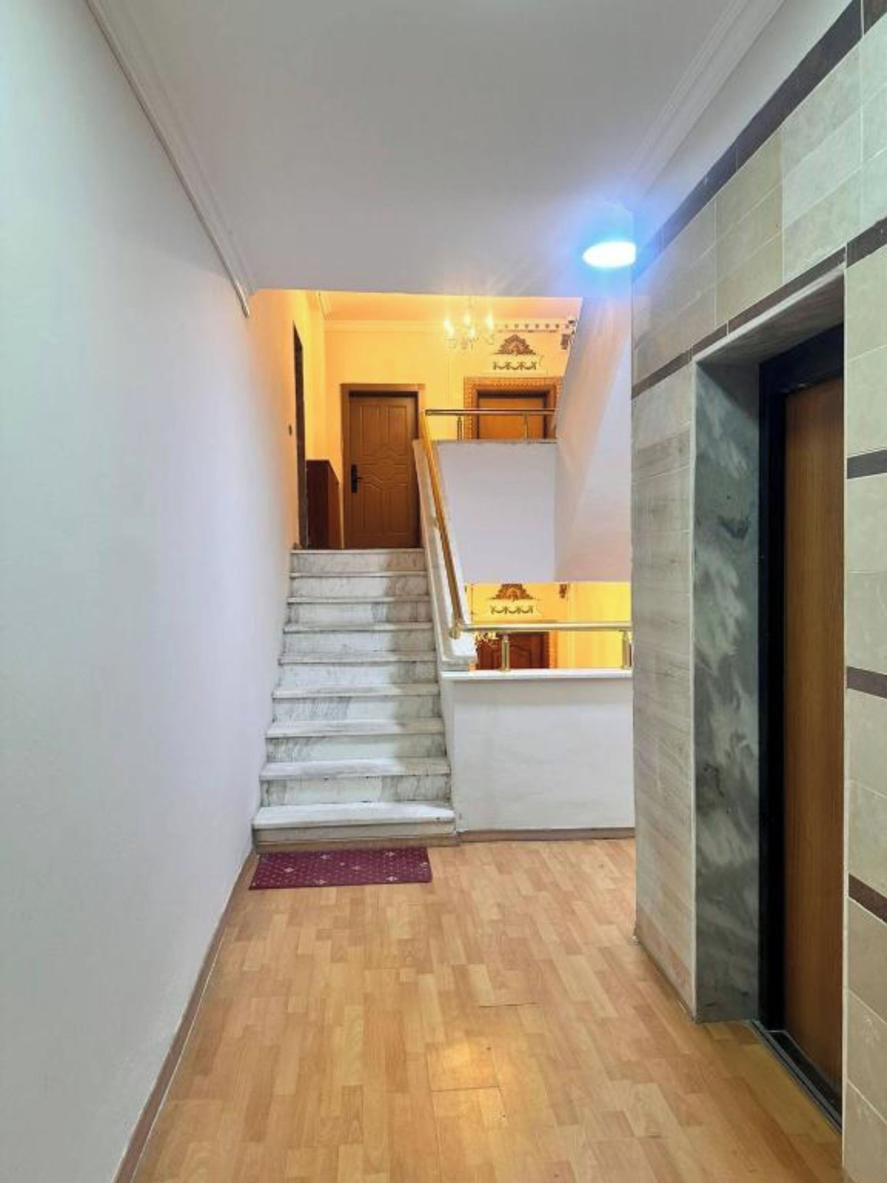 Una escalera conduce a un segundo piso con piso de madera y pared de mármol.