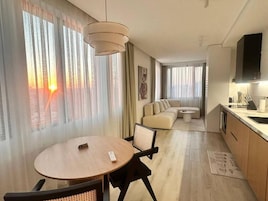 A modern hotel room with a dining area, a sofa, and a kitchen.