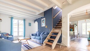 A modern living room with a staircase, a sofa, a coffee table, and a kitchen area visible through an open door. - Charming Family Holiday Home with Private Terrace and Garden (Le Grand-Village-Plage)