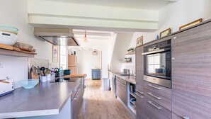 A modern kitchen with a central island, built-in appliances, and a view to the dining area. - Charming Family Holiday Home with Private Terrace and Garden (Le Grand-Village-Plage)