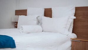 Una cama bien hecha con ropa de cama y almohadas blancas, un cabecero de madera y una mesita de noche con una lámpara.