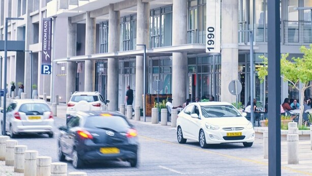 Un edificio moderno con un cartel llamativo que dice '1990', varios pisos y un estacionamiento.