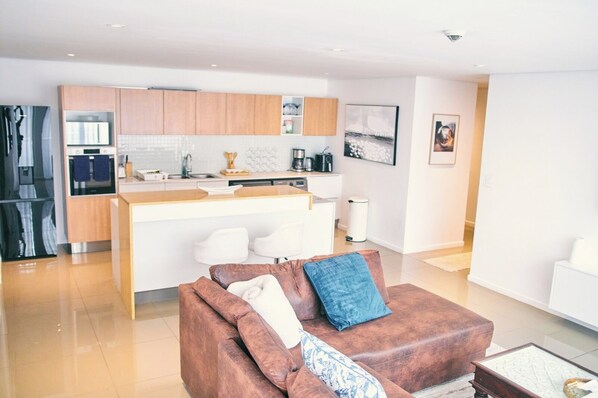 A modern kitchen with wooden cabinets, a central island, and a dining area with white chairs.