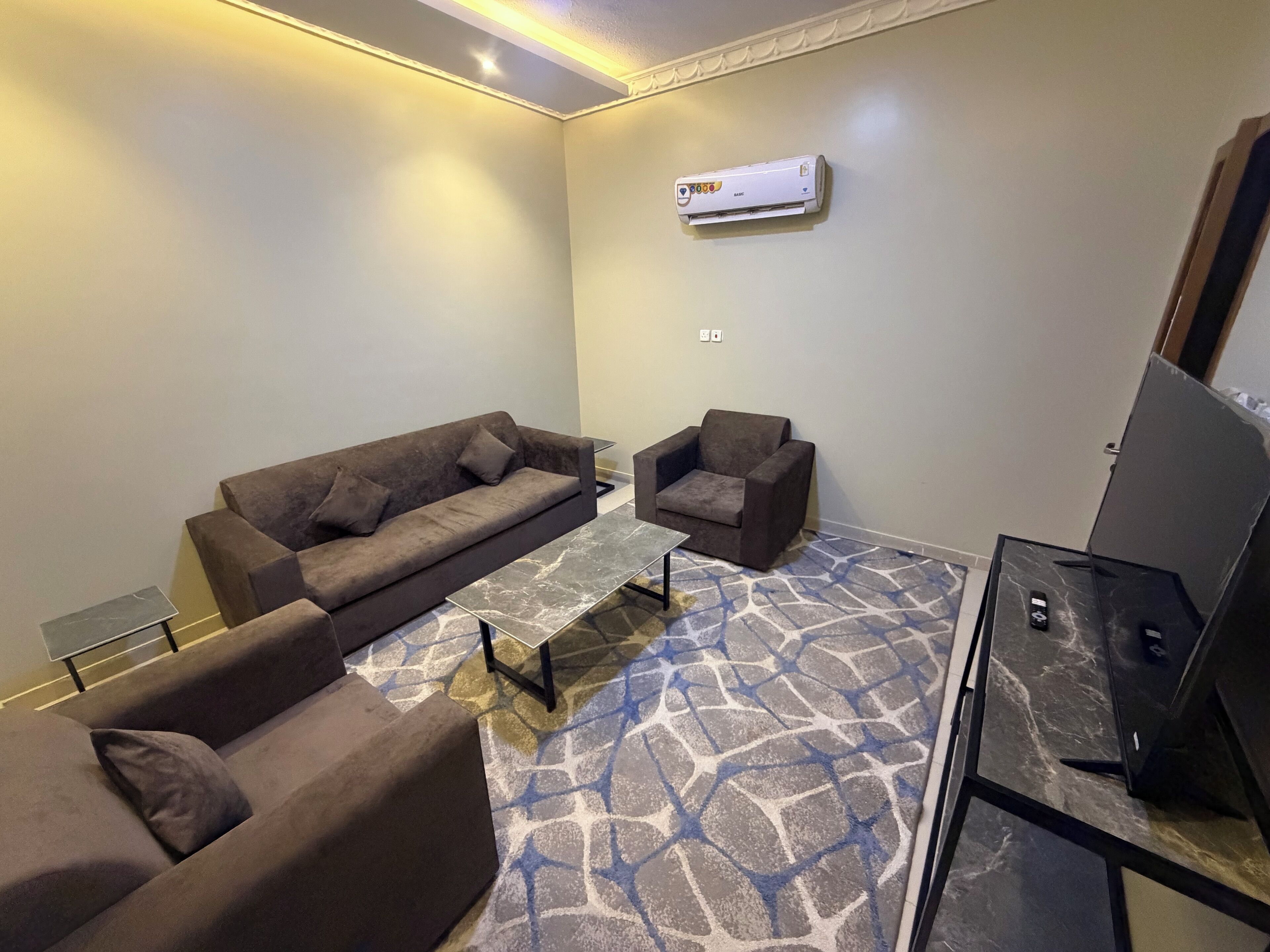 A living room with a sofa, armchair, coffee table, and a flat-screen TV on a stand.