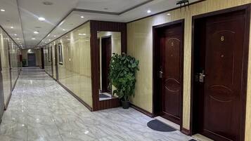 Un couloir d’hôtel avec un sol en marbre, des portes en bois numérotées 5 et 6, et une plante en pot.