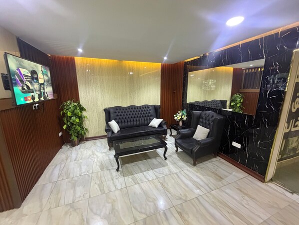 Una sala de estar moderna con un sofá negro, una mesa de centro de vidrio y un televisor de pantalla plana grande montado en la pared.