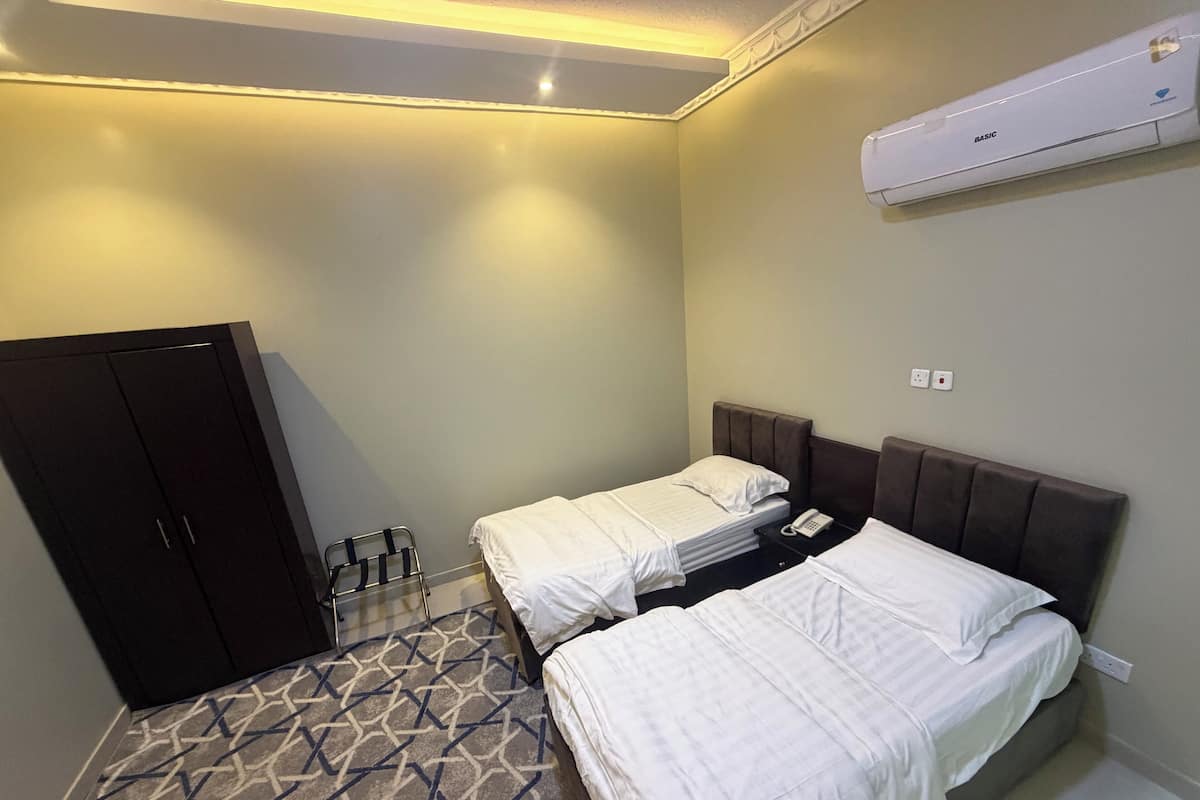 Habitación de hotel con dos camas, un armario, piso estampado y un equipo de aire acondicionado.