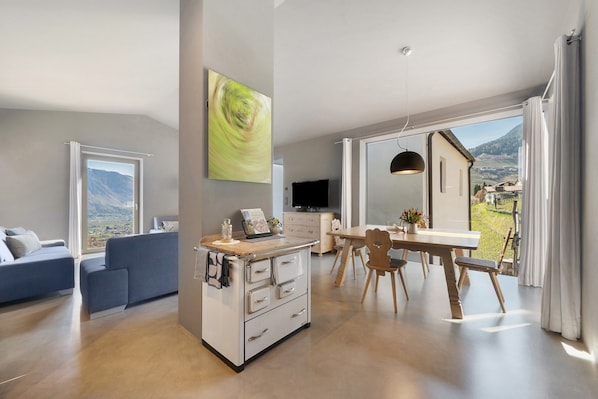 A modern kitchen with a dining area, large windows, and a view of the countryside. - Apartment Am Grübl with Mountain View, Private Terrace, and Wi-Fi (Lana)