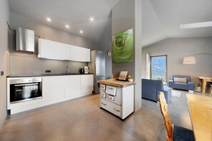 Una cucina moderna con elettrodomestici integrati, un'area pranzo con tavolo in legno e un soggiorno con divano e un grande quadro.