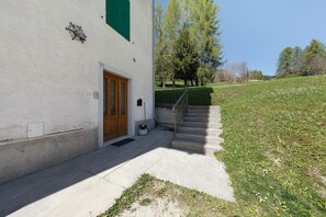 A building with a wooden door, a small outdoor area with steps leading up to a grassy hill, and a clear sky.