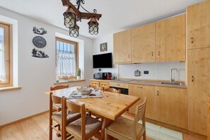 A kitchen with wooden cabinets, a dining table with chairs, a clock, and a television on the wall.