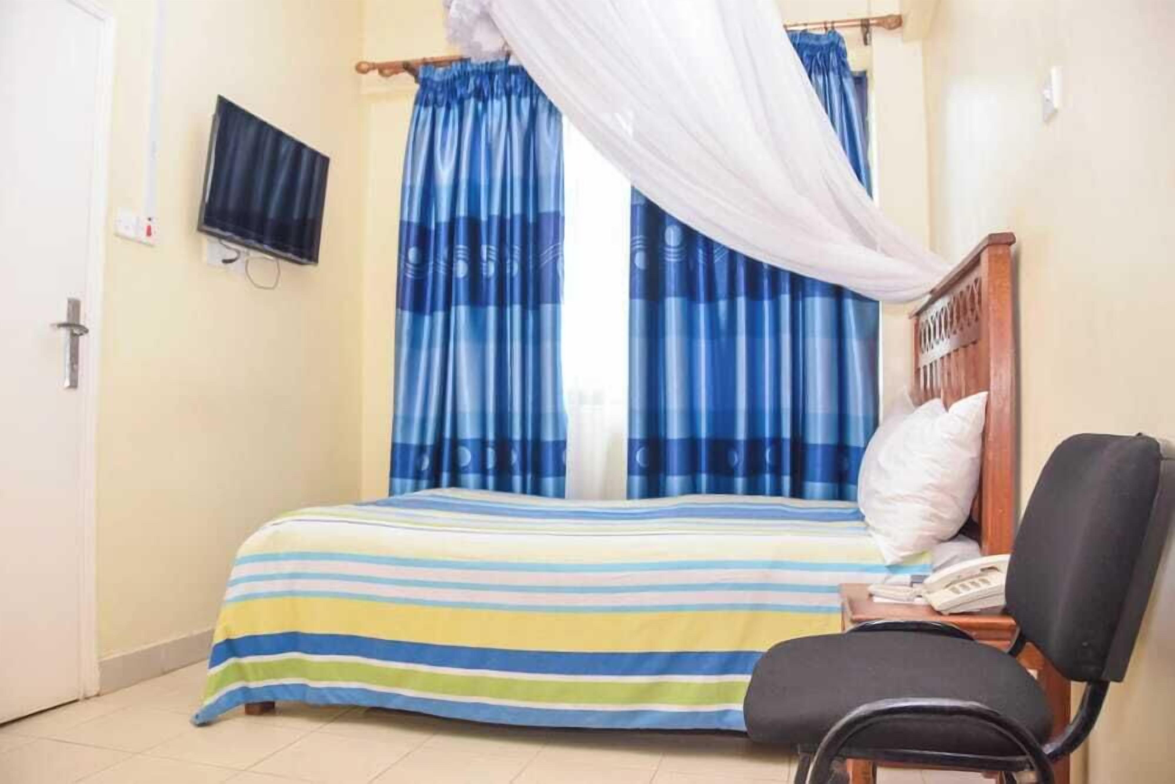 Habitación de hotel con una cama, una silla, un televisor montado en la pared y cortinas.
