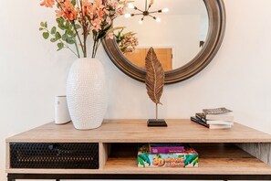 Ein hölzerner Konsolentisch mit einer weißen, strukturierten Vase, einer dekorativen Feder und einem Stapel Bücher.