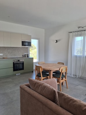 A modern kitchen with a microwave, oven, and dining area with a table and chairs. - 70 m² air-conditioned mini-villa with garden 5 minutes from beaches. (Serra-di-Ferro)