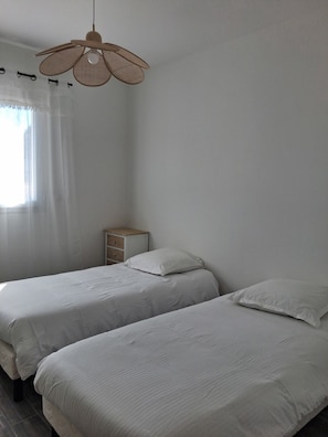 A bedroom with two beds, a bedside table, a hanging light fixture, and a window with sheer curtains. - 70 m² air-conditioned mini-villa with garden 5 minutes from beaches. (Serra-di-Ferro)