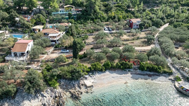 Vista aérea de una propiedad costera con varias casas, una playa despejada y terreno rocoso.