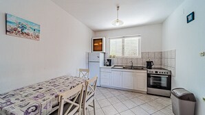 Una cocina compacta con armarios blancos, una estufa, un fregadero y una ventana con persianas.