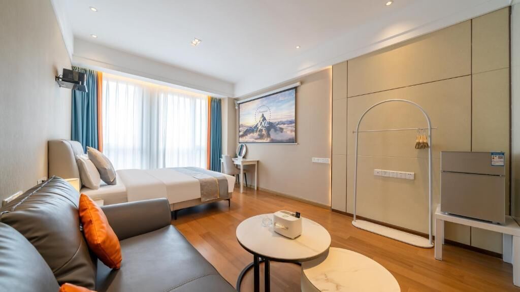 Quarto de hotel moderno com cama, sofá, TV e área de chuveiro.