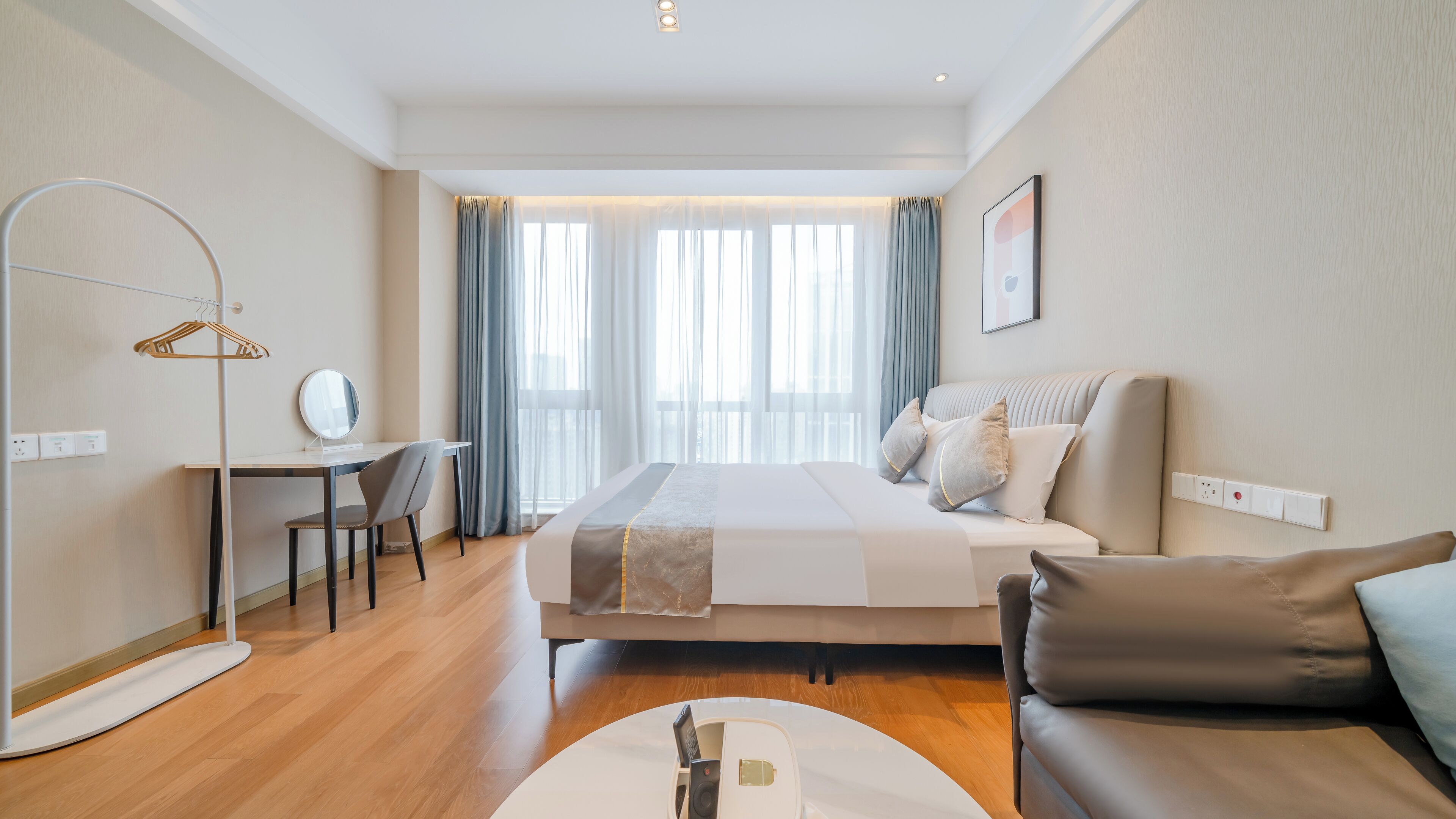 Una habitación de hotel moderna con cama, escritorio, silla, perchero y sofá.