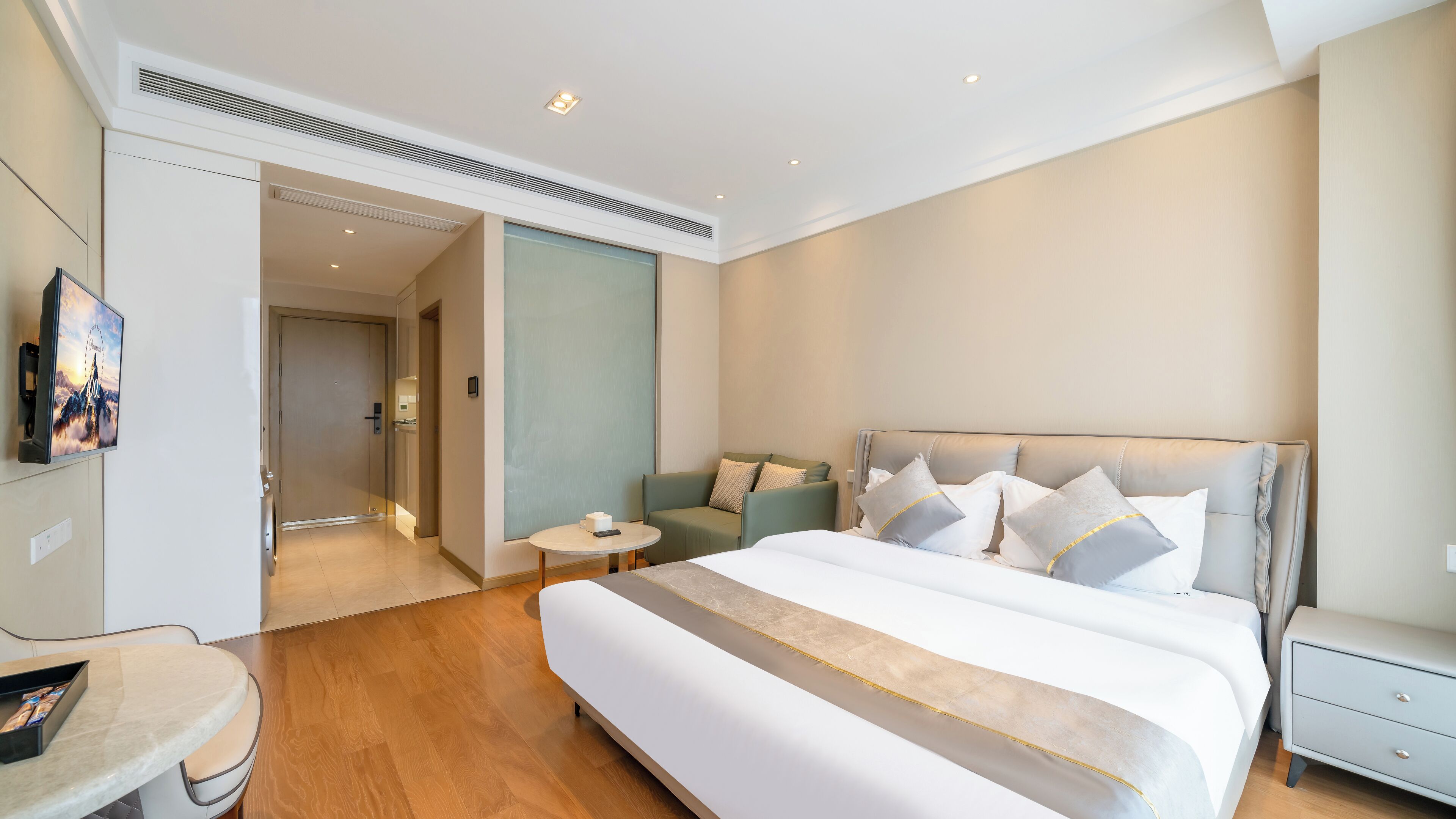 A modern hotel room with a large bed, a seating area, and a television on the wall.
