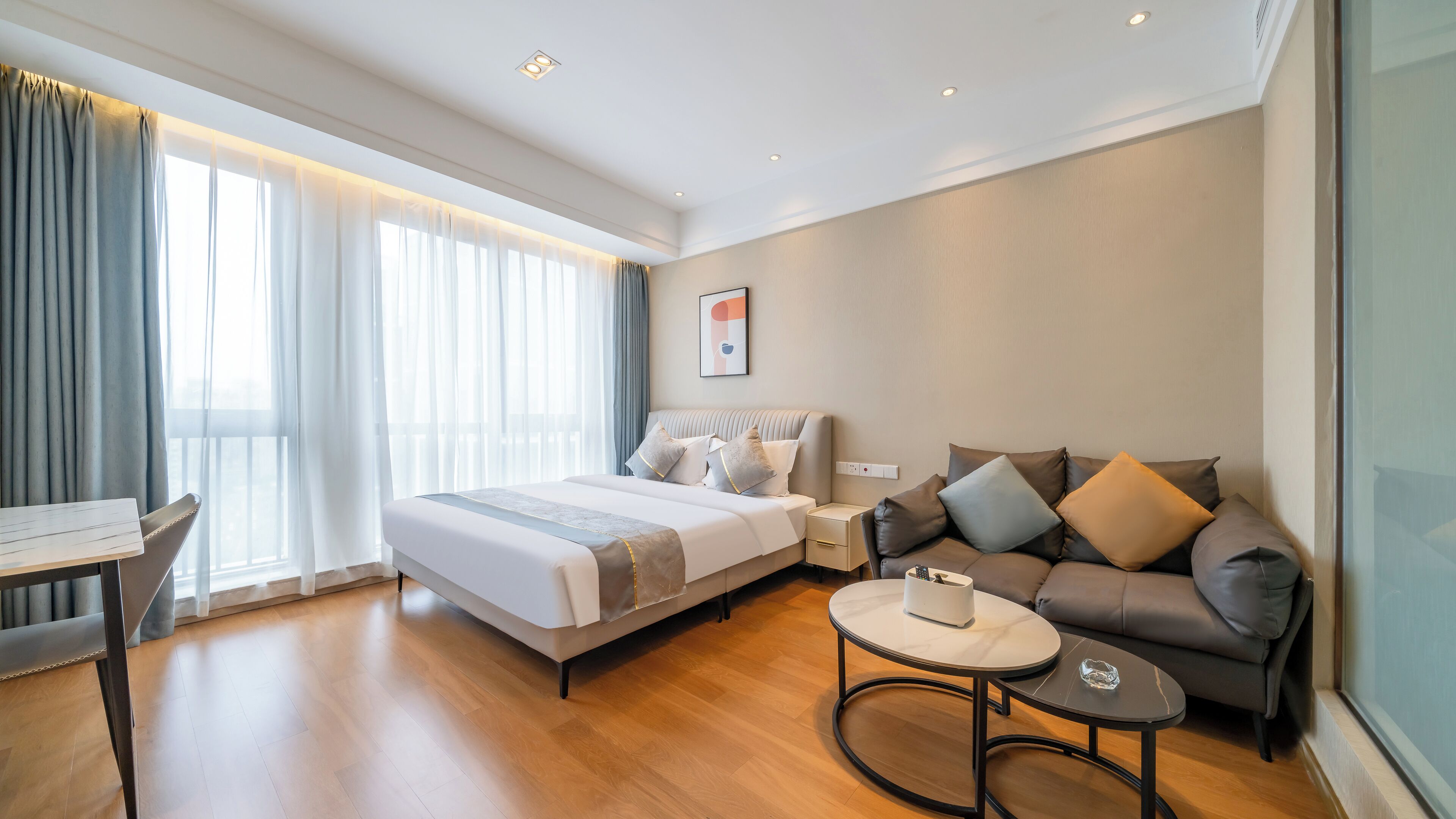 A modern hotel room with a large bed, a sofa, a small table, and a desk.