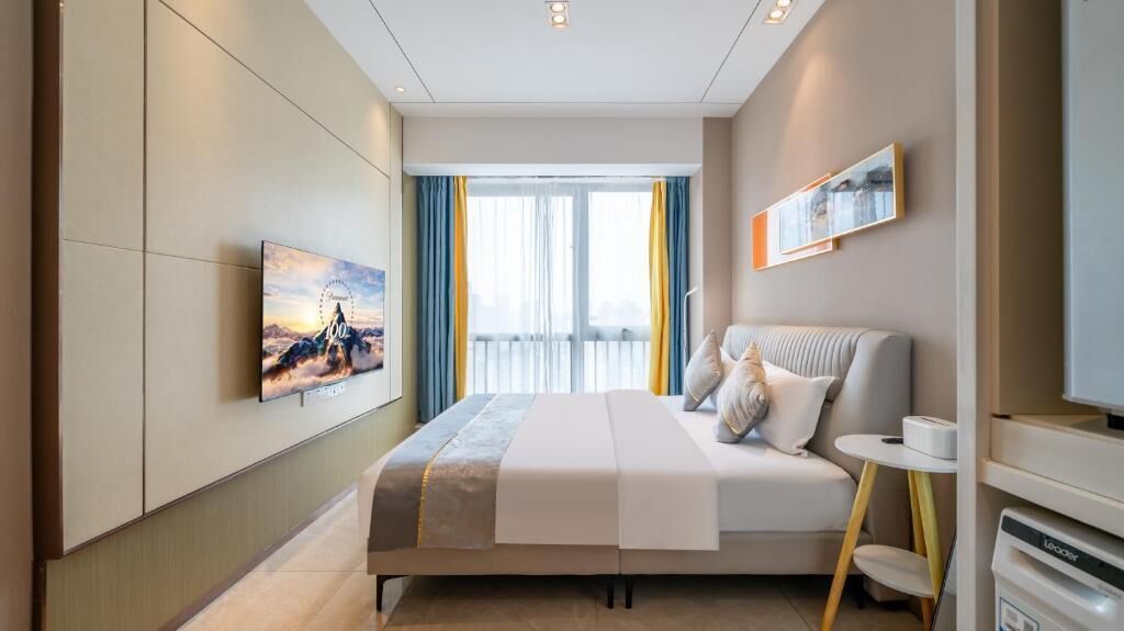 A modern hotel room with a bed, a bedside table, a window with curtains, and a wall-mounted picture.