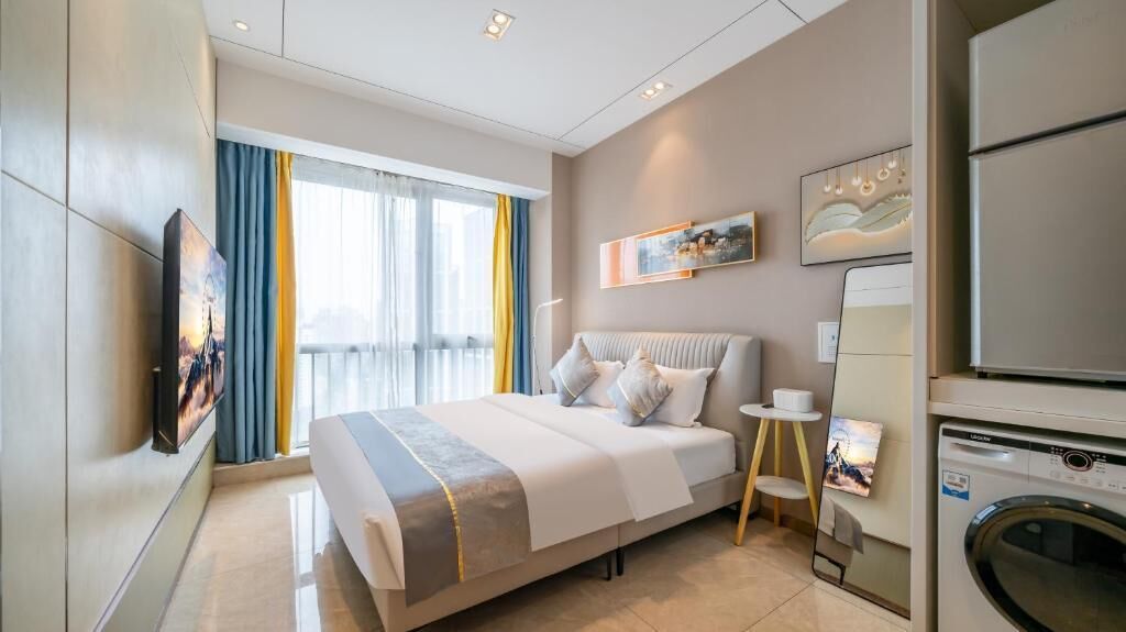Une chambre d’hôtel moderne dotée d’un grand lit, d’un téléviseur à écran plat fixé au mur, d’une machine à laver et d’une fenêtre avec des rideaux.