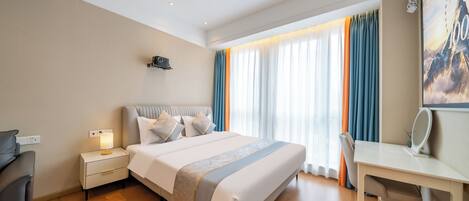 A hotel room with a bed, bedside table, lamp, desk, chair, and a large window with curtains.