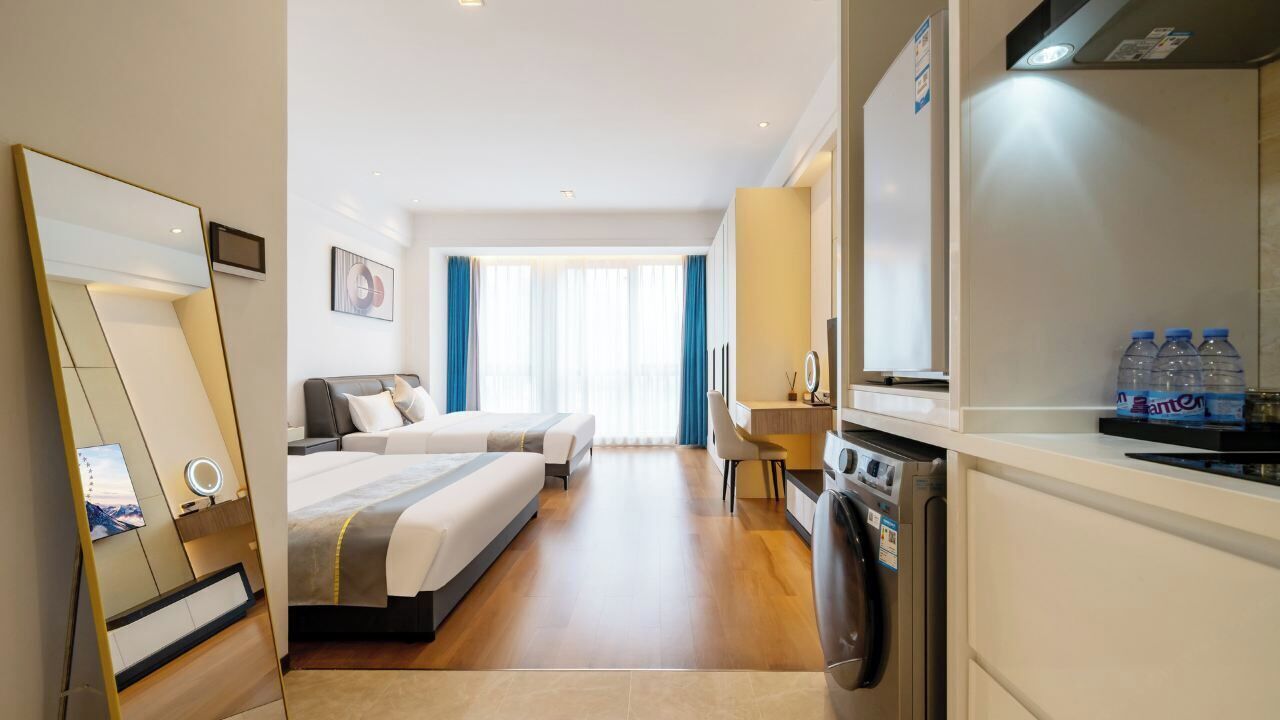 Habitación de hotel con dos camas, un espejo grande, un escritorio con silla, lavadora y refrigerador.