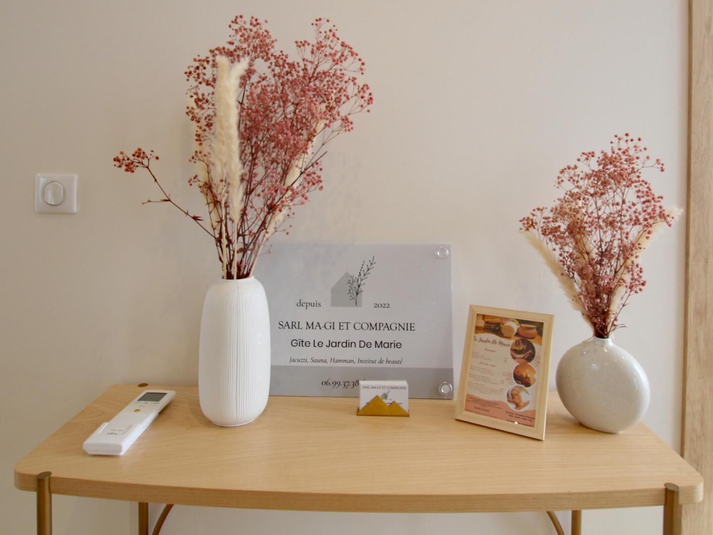 Una mesa de madera con un jarrón blanco, un certificado enmarcado, un pequeño objeto en forma de pirámide y un dispositivo digital.