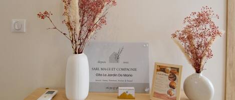 Una mesa de madera con un jarrón blanco, un certificado enmarcado, un pequeño objeto en forma de pirámide y un dispositivo digital.