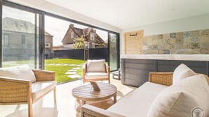 Een moderne buitenruimte met rieten meubilair, een jacuzzi en een uitzicht op een traditioneel huis op de achtergrond.