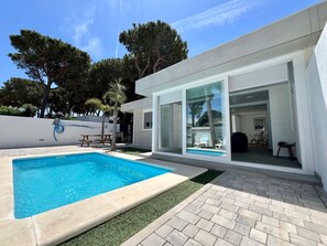 Una casa moderna con piscina, un patio y una puerta de vidrio que da a una zona de estar al aire libre.