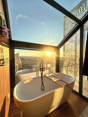 Ein modernes Badezimmer mit freistehender Badewanne, großen Fenstern und Blick auf die Stadt.
