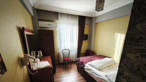 A hotel room with a bed, a desk with a telephone, a chair, and a small table with a glass. - Yılay Otel (Igdir)