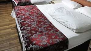 A hotel room with four single beds, each with a red floral bedspread and white pillows. The room has yellow walls, a wooden floor, and a white ceiling with decorative molding. - Yılay Otel (Igdir)