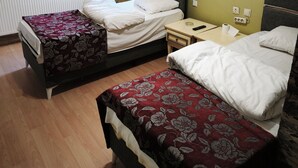 A hotel room with two beds, a radiator, a window with curtains, a bedside table with a remote control, and a power outlet. - Yılay Otel (Igdir)
