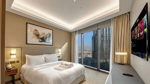 Een hotelkamer met een groot bed, een bureau, een televisie en uitzicht op de stad.