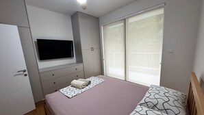 Ein Schlafzimmer mit einem Bett, einem an der Wand montierten Fernseher, einem Fenster und einem Deckenventilator.