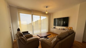 Ein Wohnzimmer mit einer Couch, einem Couchtisch und einem an der Wand befestigten Fernseher.